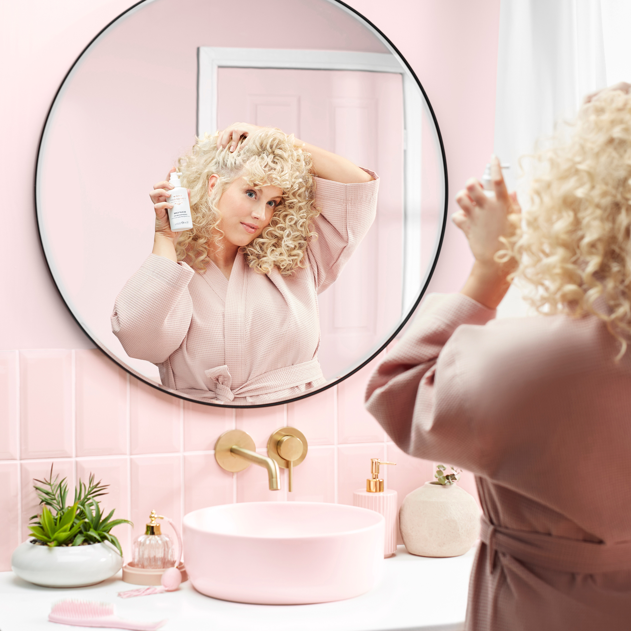 Blonde woman admires her curls in pink bathroom mirror